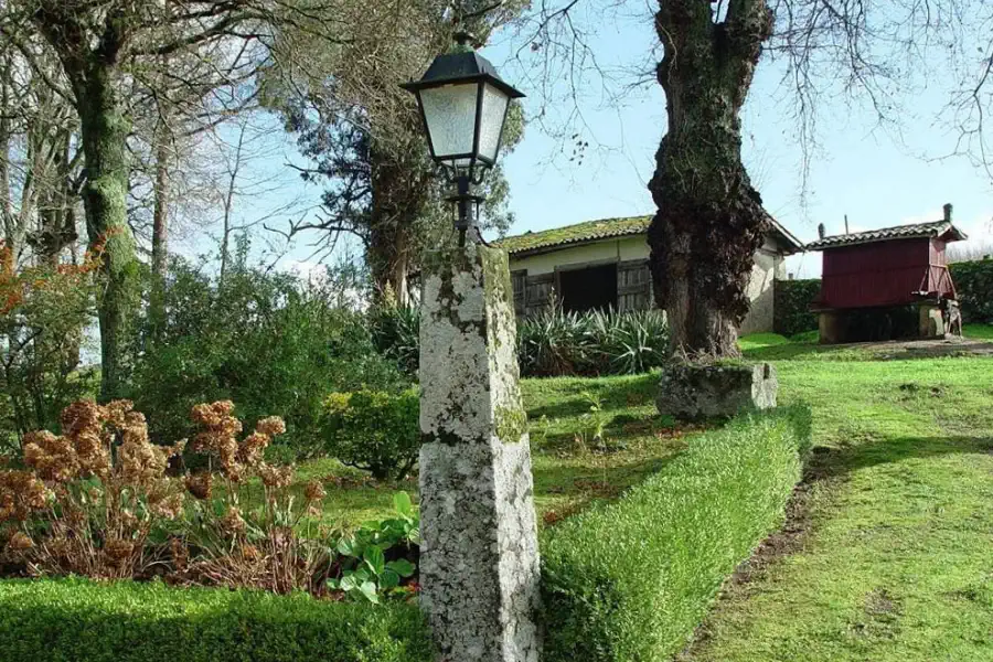 The estate gardens with a stone lantern post, a rusticated outbuilding and a traditional Galician hórreo in the background.